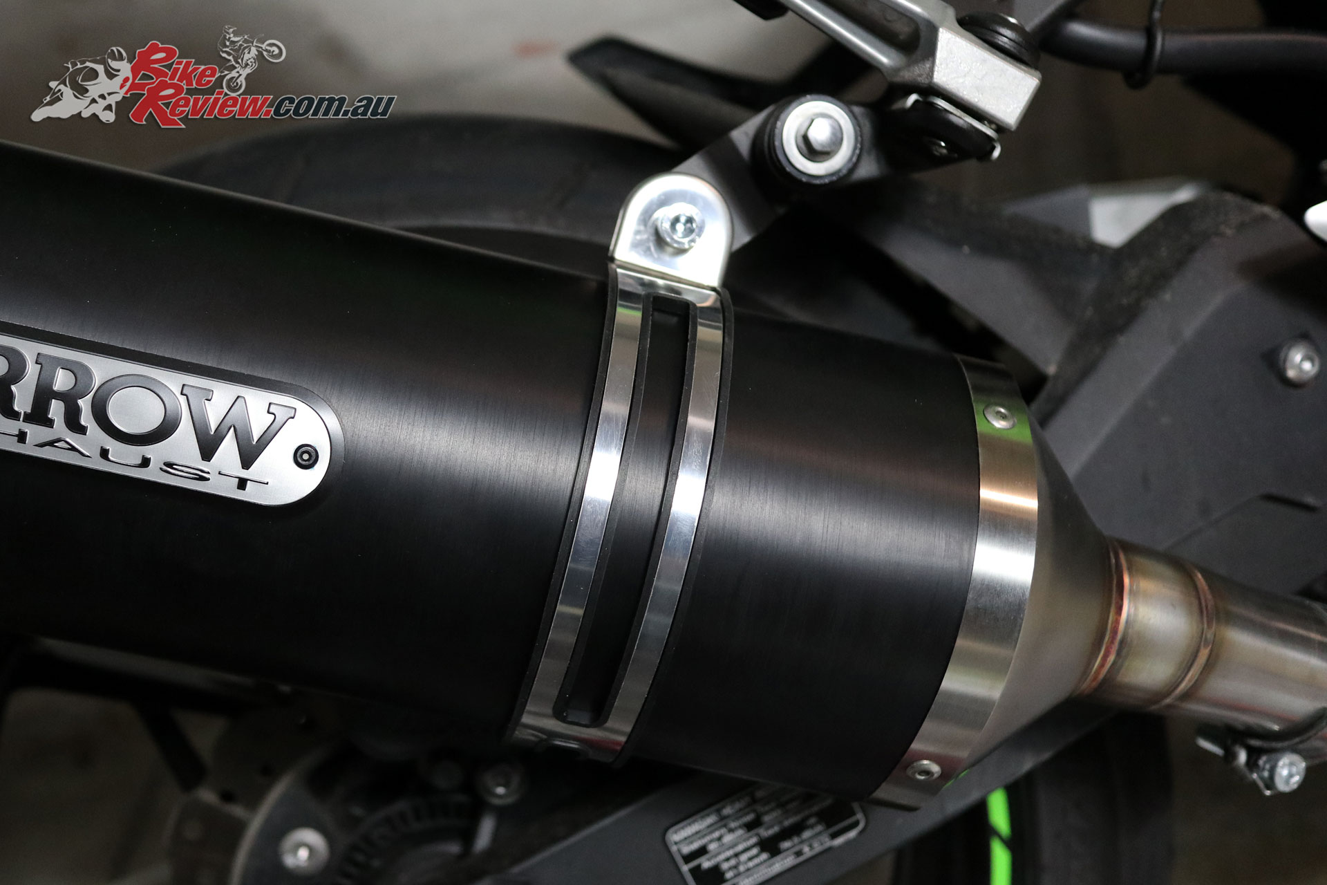 See here the black bracket mounted to the pillion peg hanger, as well as the exhaust clamp