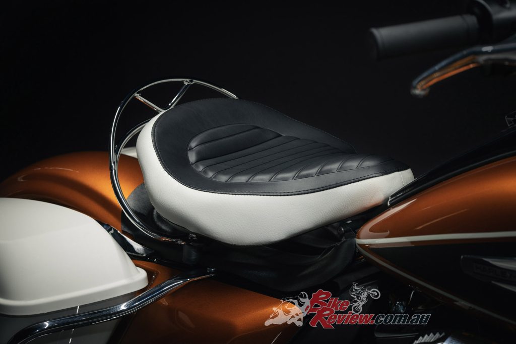 "A solo saddle with a black-and-white cover and a chrome rail, mounted over an adjustable coil spring and shock absorber"...